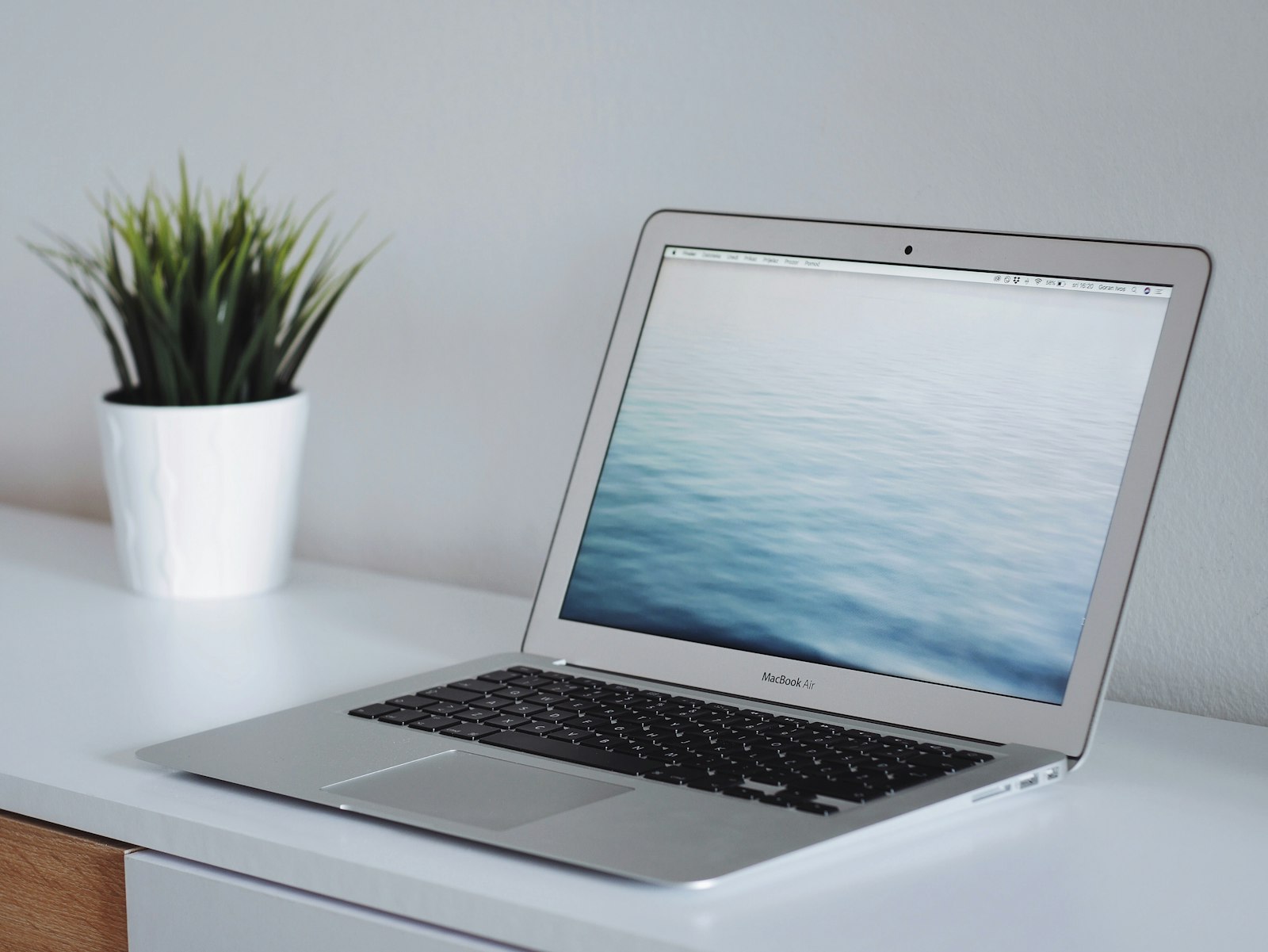 Laptop naast een groene plant op een houten bureau, symbool voor website en browsergebruik